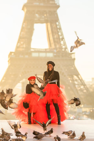 A vertical shot of a Black mother with her daughter in front of the Eiffel Tower