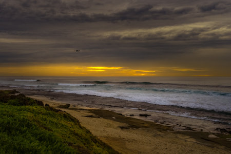 THE LAJOLLA SHORELINE WITH A SAND AND ROCK SHORELINE AND NICE WAVES, SURFERS AND A HELICOPTER IN THE...
