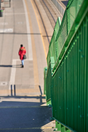 A vertical shot of a green metal fence with an out of focus woman walking on the street in the backgroundの写真素材