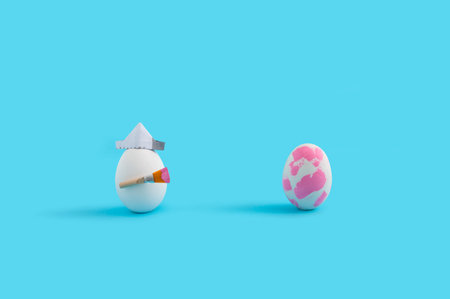 The two painted eggs with paintbrush and paper hat isolated on a blue background with free space for...