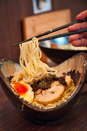A closeup of a hand holding chopsticks with noodles in a Japanese restaurantの写真素材
