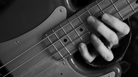 A closeup grayscale of a hand holding a chord on the bass guitar - for backgroundsの写真素材