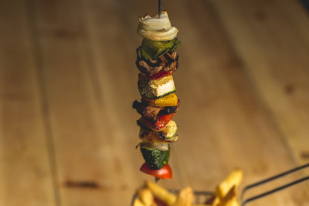 A Closeup of a hanging kebab ( grilled meat with vegetables ) served with French friesの写真素材