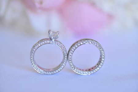 A closeup of two white diamond wedding rings on a white blurry background