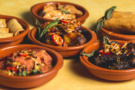 A closeup of fried meat with vegetables and rolls served in a clay bowl on a food tableの写真素材