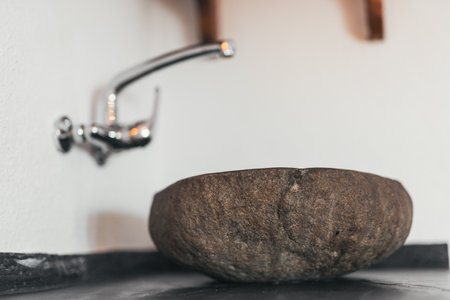 A close-up shot of a sink made of rocks with a stainless tap on a white wall in blurred backgroundの写真素材