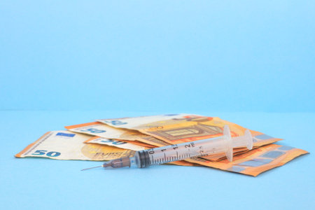 A closeup shot of money and syringe isolated on the blue backgroundの写真素材