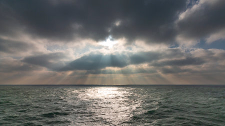 A mesmerizing view of the sunlight penetrating through the clouds over the wavy sea waterの写真素材