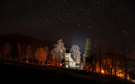 A picturesque view of a mountain forest lit by the red lights of the houses on a starry night sky backgroundの写真素材