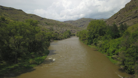 A river surrounded by trees and hills on a cloudy day