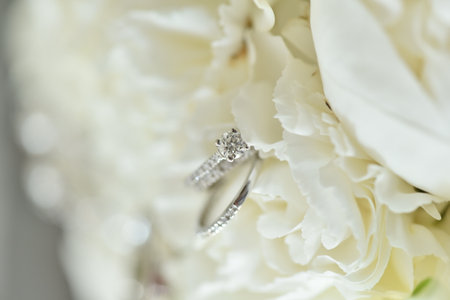 A shallow focus of two diamond wedding rings on a white flower decoration backgroundの写真素材