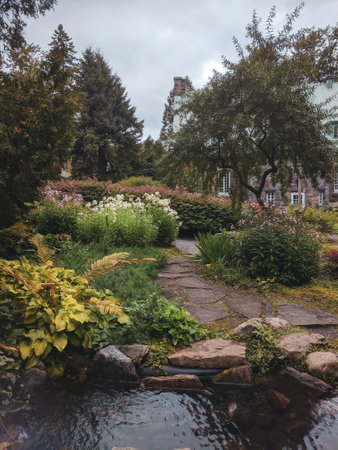 A shallow pool in a garden surrounded by thick bushes of colorful flowers and lush trees on a gloomy dayの写真素材