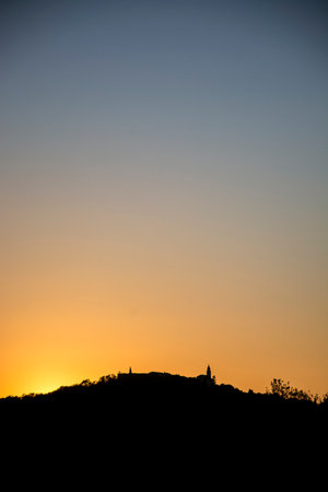 A vertical shot of a silhouette of the small town on the hill with the sunset on the backgroundの写真素材