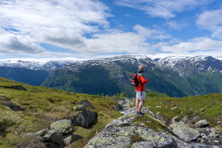 A view of a mountain climber on top of the hill with a backpack on a sunny dayの写真素材