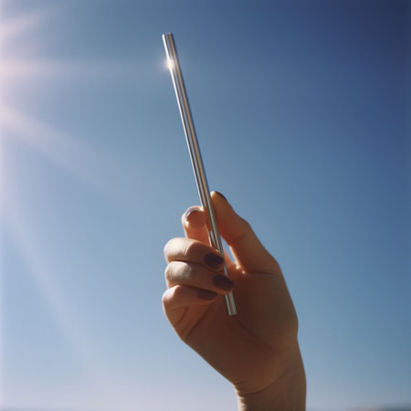 A human hand holding a metal straw towards the sky, illuminated by sun rays - AI generatedの素材