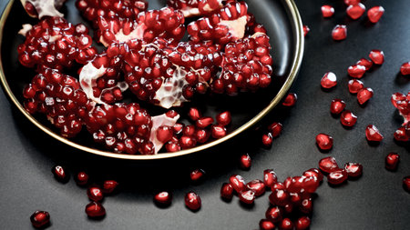 An AI generated illustration of close-up of fresh, vibrant pomegranates in a glossy black plate, ready to be eatenの素材