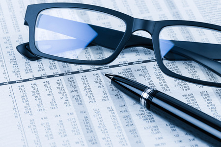 Pen and glasses rest on stock price detail financial newspaperの写真素材