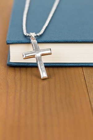Necklace with silver cross on wooden table and blue bible bookの写真素材