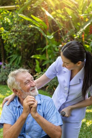 Happy nurse take care elderly man on wheelchair in garden at nursing homeの写真素材