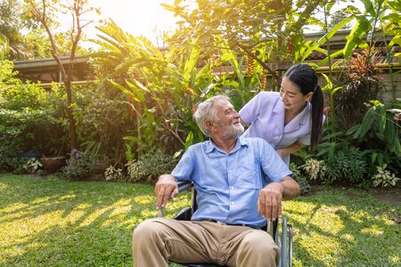 Happy nurse take care elderly man on wheelchair in garden at nursing homeの写真素材
