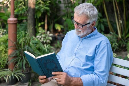 Senior elderly man reading book in gardenの写真素材
