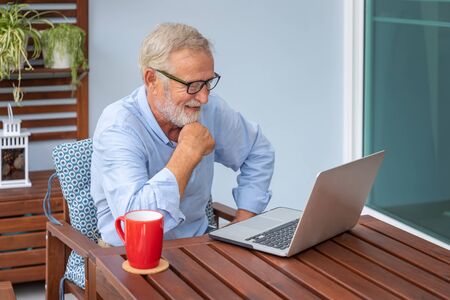 Senior man executive with white hair using computer laptop watching movie at home with coffeeの写真素材