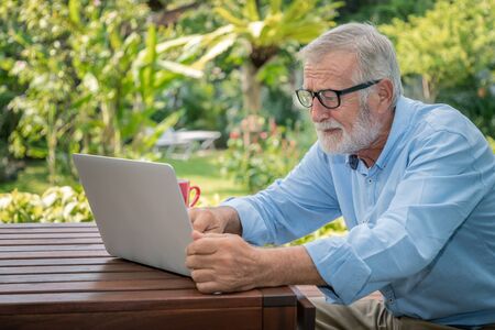 Senior man executive with white hair using typing computer laptop working at home with coffeeの写真素材