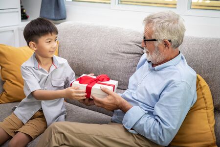 Happy boy grandson playing with old senior man grandfather at home with presentの写真素材