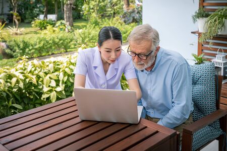 Caregiver assist senoir eldery man using notebook laptop computer connect to Internetの写真素材