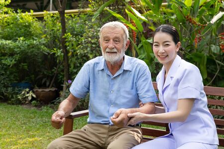 Happy nurse holding elderly man hand in garden at nursing home looking cameraの写真素材