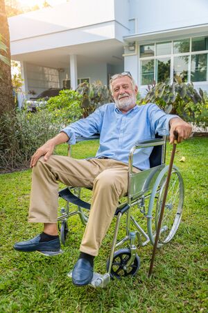 Happy senior old caucasian man holding cane sitting on wheelchai in gardenの写真素材
