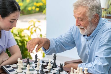 Elderly playing chess with nurse caregiver in nursing home for leisureの写真素材
