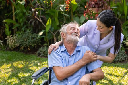 Happy nurse take care elderly man on wheelchair in garden at nursing homeの写真素材