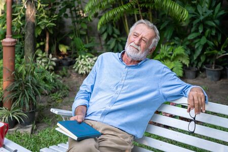 Senior elderly man holding book with breakfast and mug of coffee in gardenの写真素材