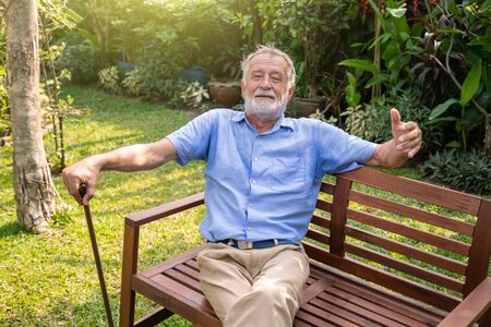 Happy senior old caucasian man holding cane sitting on bench in gardenの写真素材