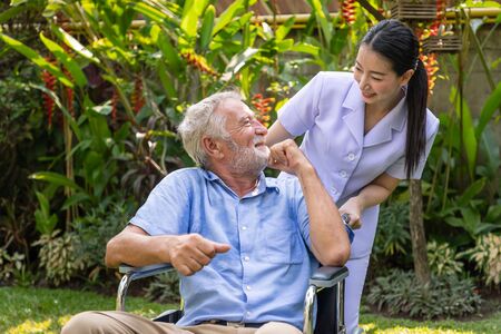 Happy nurse take care elderly man on wheelchair in garden at nursing home with thumb upの写真素材