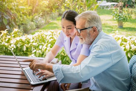 Caregiver assist senoir eldery man typing using notebook laptop computer connect to Internetの写真素材