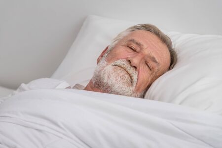 Senior elderly man sleeping with white blanket in bedroomの写真素材