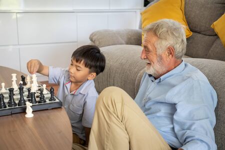 Happy boy grandson playing chess with old senior man grandfather at homeの写真素材