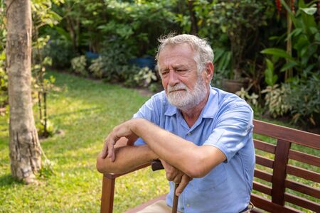 Thoughtful senior old caucasian man holding cane sitting on bench in gardenの写真素材