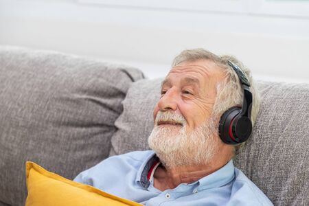 Senior old man eldery enjoy listening to music with headphone on couch sofaの写真素材