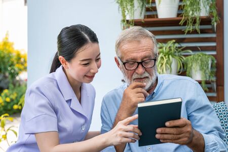 Senior elderly man reading book with nurse in gardenの写真素材