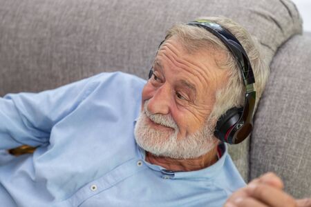 Senior old man eldery enjoy listening to music with headphone on couch sofa