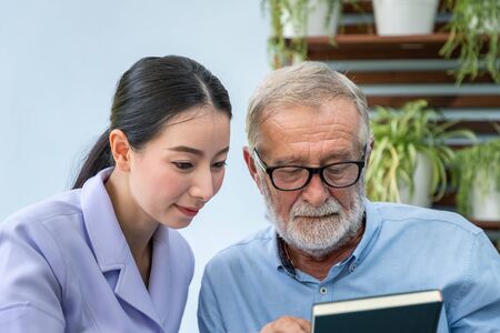 Senior elderly man reading book with nurse in gardenの写真素材