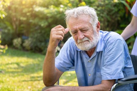 Depressed thoughtful elderly man on wheelchair with nurse in garden at nursing homeの写真素材