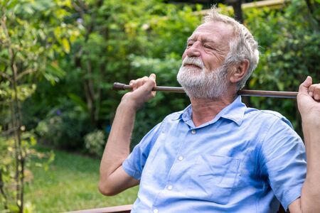 Thoughtful depressed senior old caucasian man holding cane with two hands sitting in garden