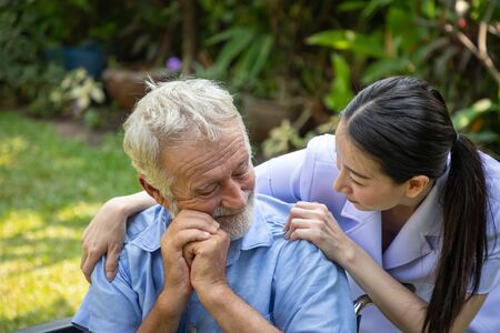 Nurse take care and comfort elderly man on wheelchair in garden at nursing homeの写真素材
