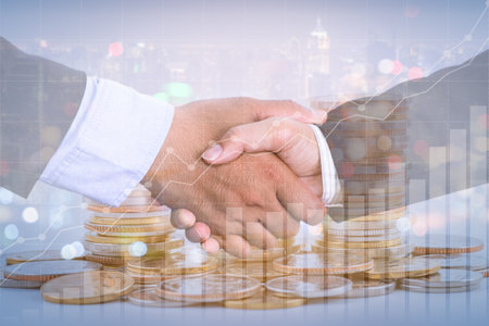 Successful cooperative, teamwork, and joint venture concept; double exposure of handshake and coins stack, with growing trend graph.の写真素材