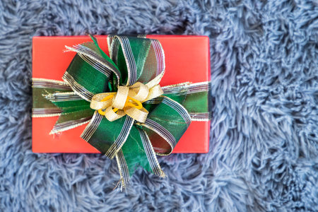 Red present gift box with green ribbon on grey shaggy fur carpet backgroundの写真素材