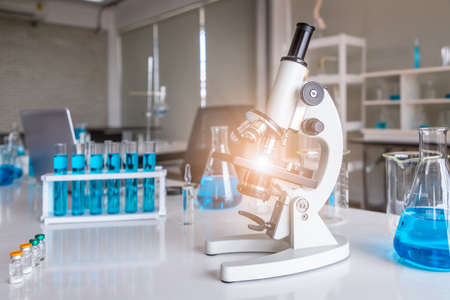 Microscope examining slide of sample with test tubes in background. Concept for science and technology research in laboratory.の写真素材
